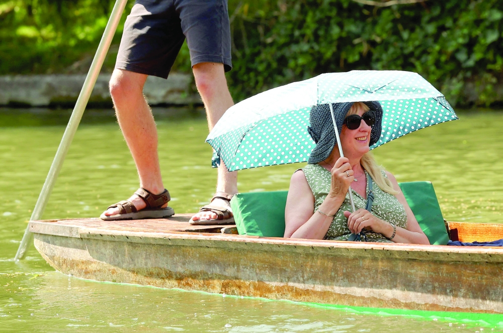A person shelters from the sun beneath a parasol as they take a punt ride along the River Cam, during a heatwave, in Cambridge on Wednesday. — AFP