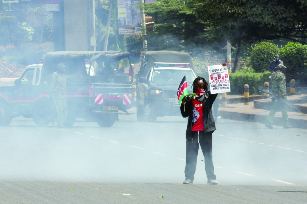 A demonstrator holds a placards as police officers use tear gas to disperse protesters, in Nairobi. — Reuters 