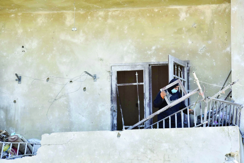 
A Lebanese woman removes broken metal railing from her damaged house in the southern Lebanese village of Srifa. — AFP 
