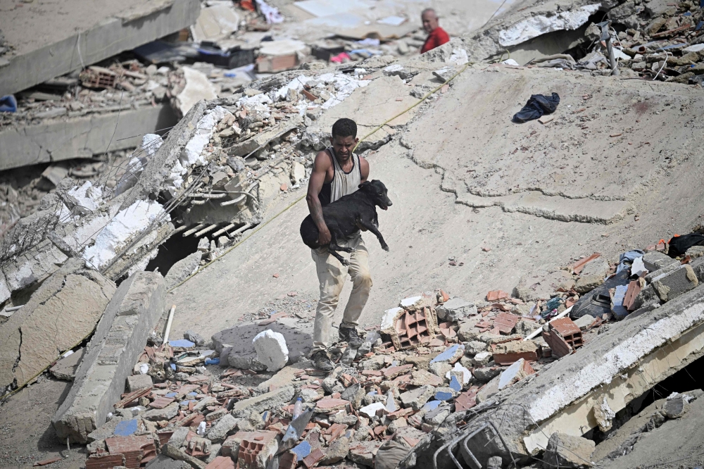 A volunteer carries a rescued dog across the rubble of a collapsed building following twin earthquakes in Caraballeda