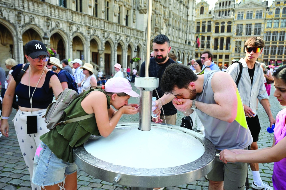Tourists drink water from a public fountain at the Grand-Place, during a heatwave in Brussels. — AFP 
