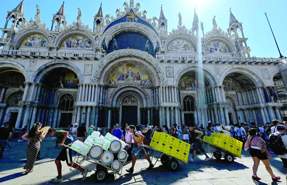 Workers push handcart loaded with water bottles during a heatwave in Saint Mark square in Venice. — AFP
