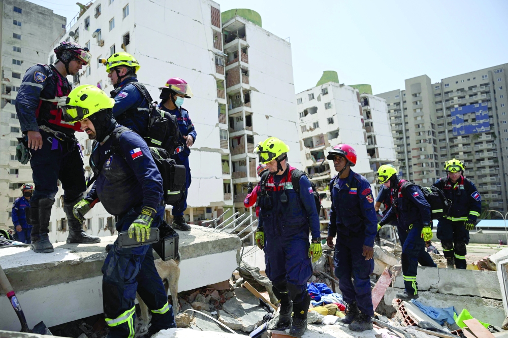 Members of Chile's USAR search and rescue team stand on rubble of damaged buildings Catia La Mar, La Guaira state. — AFP