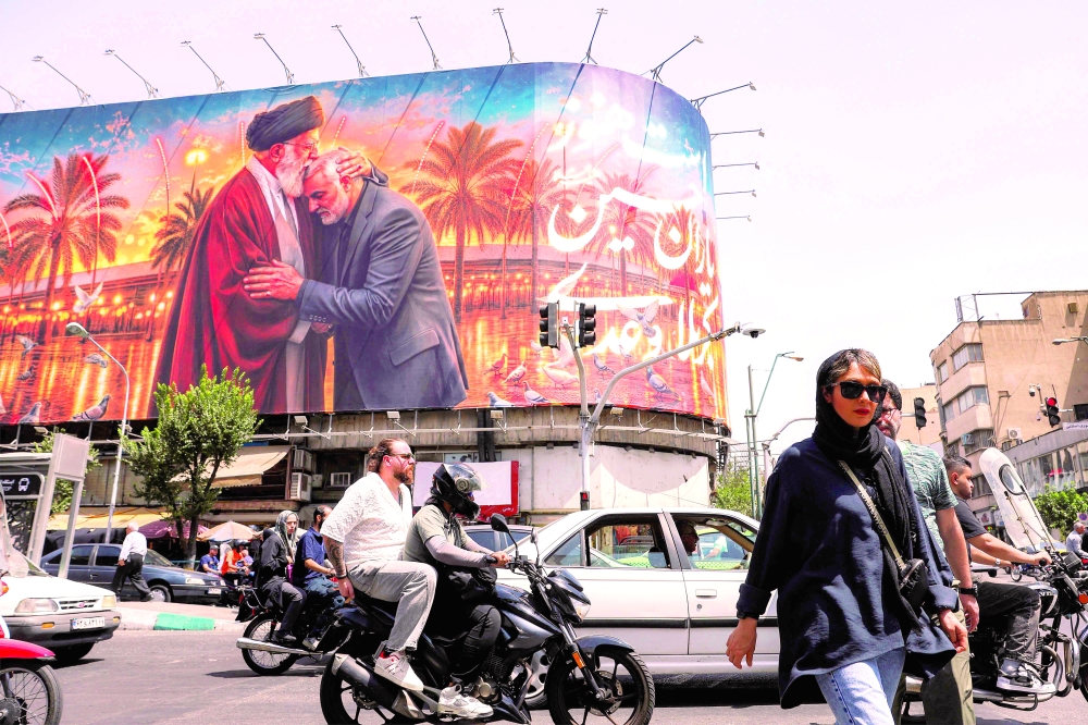 People cross a street past a billboard displayed on the facade of a building in Tehran. — AFP
