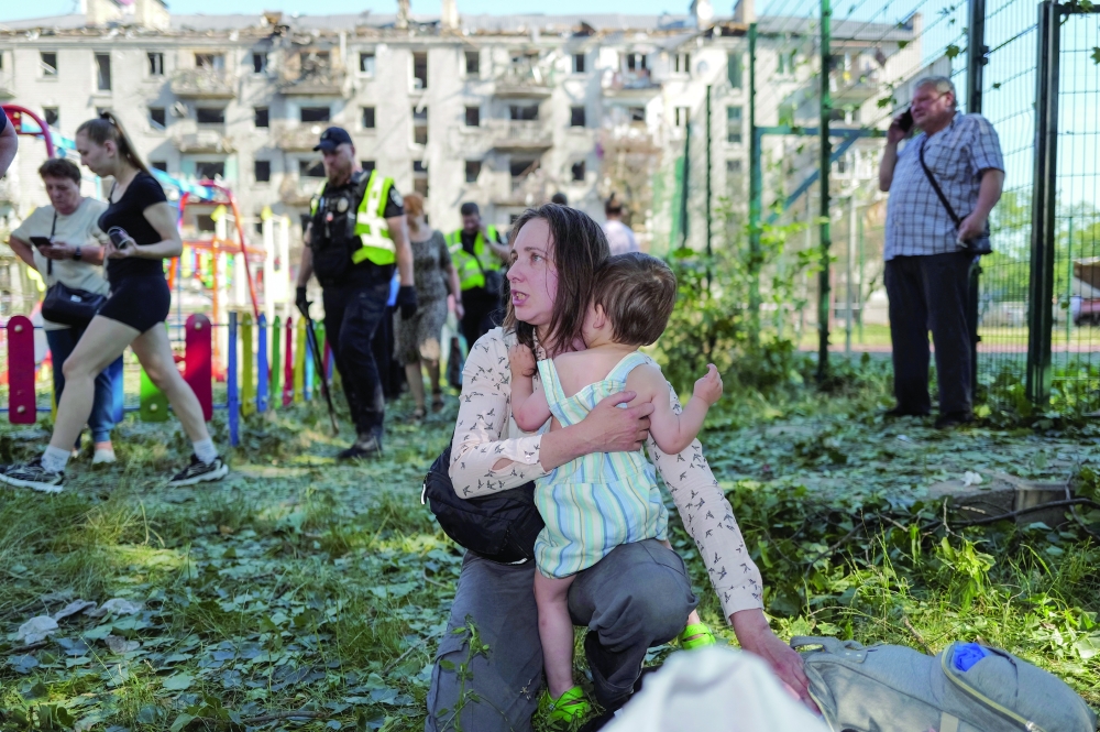 
A woman holds a child, near an apartment building damaged during a Russian missile and drone strike on Kyiv on Thursday. — Reuters 