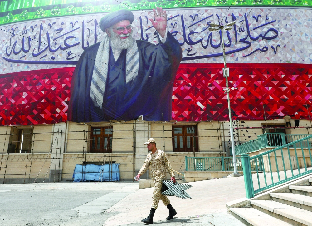 
A member of the Basij paramilitary forces carries metal parts underneath a large banner depicting Iran’s late Supreme Leader Ayatollah Ali Khamenei during preparations for a farewell ceremony for Iran’s late Supreme Leader at the Imam Khomeini Grand Mosalla, in Tehran on Thursday. — Reuters 