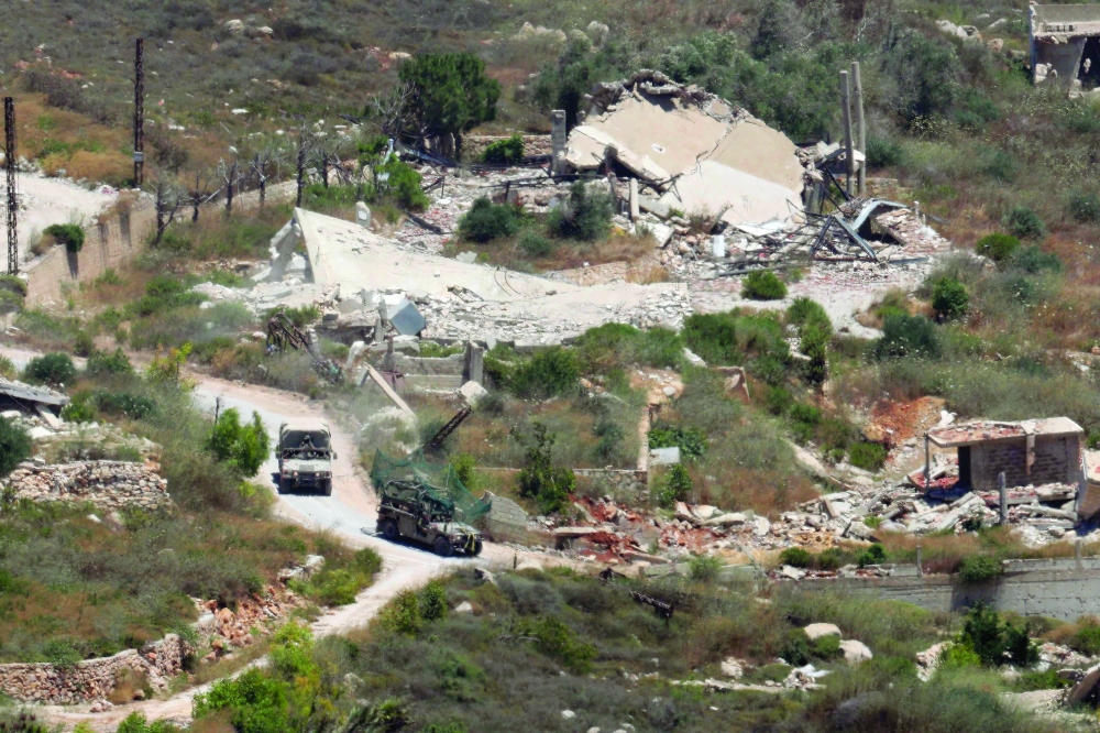 Picture taken from a position in the Upper Galilee in northern Israel shows Israeli military vehicles driving past houses destroyed in strikes in the southern Lebanese village near the Israel-Lebanon border. 
- AFP