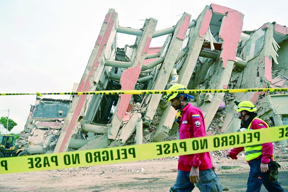 Rescue workers walk past a collapsed building cordoned off with tape, La Guaira state. — AFP