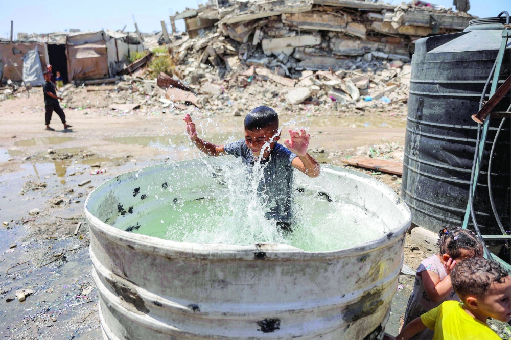 A boy plays while bathing in a giant container filled with water next to a cistern at a camp for people displaced by war in the Sheikh Radwan neighbourhood of Gaza City. - AFP