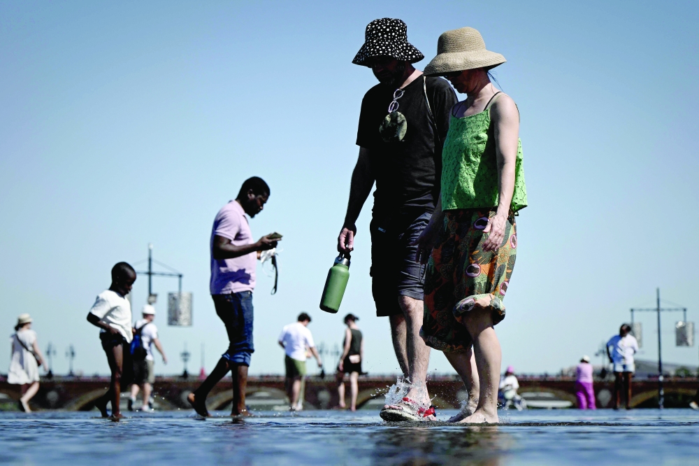 Pedestrians holding a bottle walk in the Miroir d'eau reflecting pool on the banks of the Garonne river, during a summer heatwave in Bordeaux, south-western France, on July 6, 2026. For the third time in six weeks, France is facing a surge in temperatures, with three-quarters of the country under a heatwave alert on July 7, 2026, just a few days after a historic heatwave. (Photo by Philippe LOPEZ / AFP)