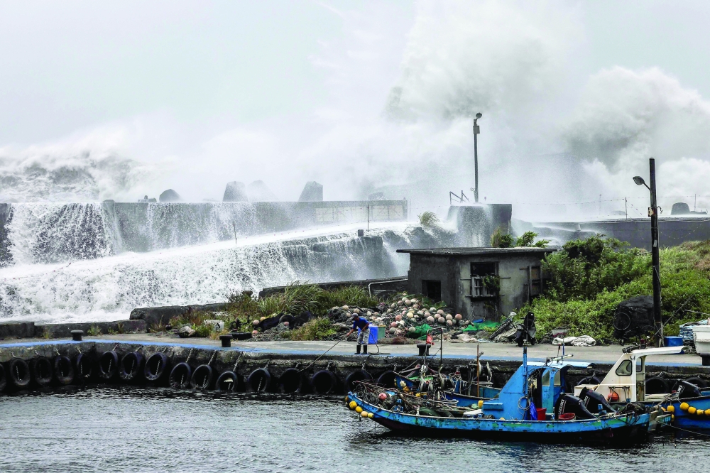A fisherman handles a rope near a fishing boat as waves crash over a breakwater in Yilan as Typhoon Bavi moves towards northeastern Taiwan. — AFP