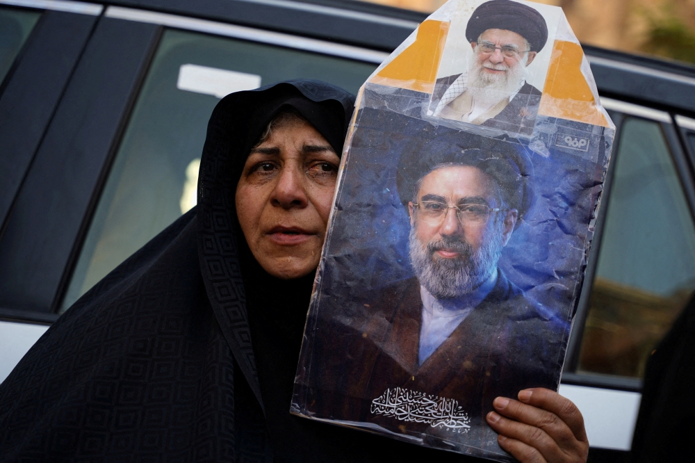 A woman holds a portrait of Iran's Supreme Leader Mojtaba Khamenei and Iran’s late Supreme Leader Ayatollah Ali Khamenei
