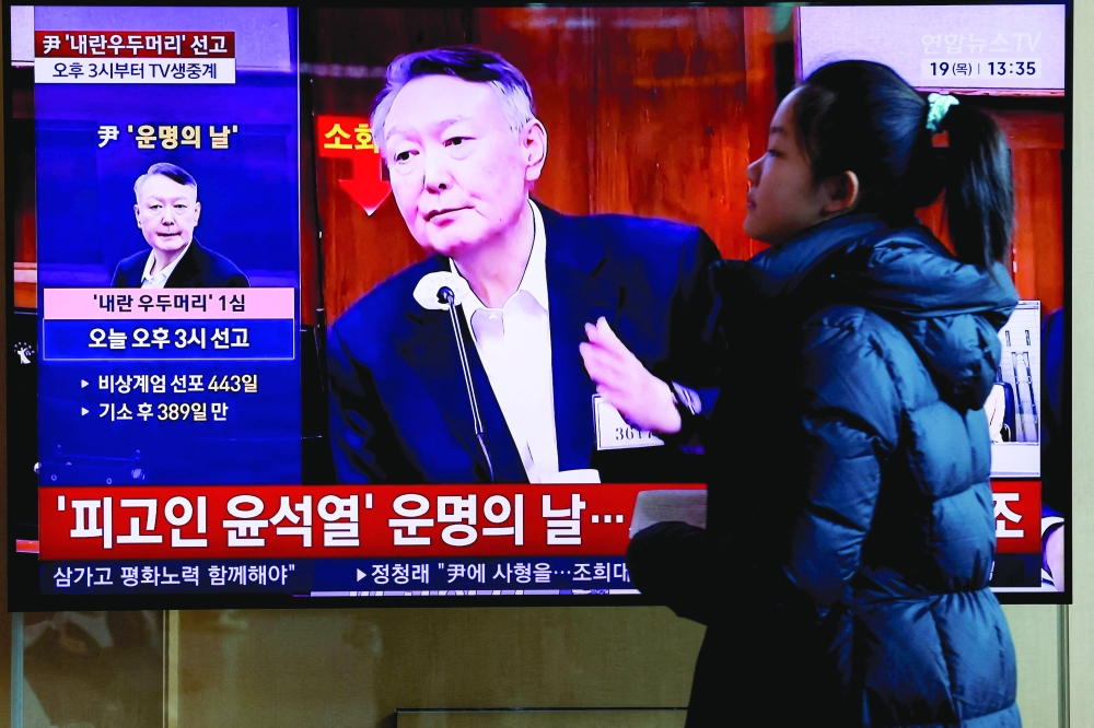 A woman walks in front of a TV screen broadcasting a news report on the sentencing trial of South Korean former president Yoon Suk Yeol. — Reuters