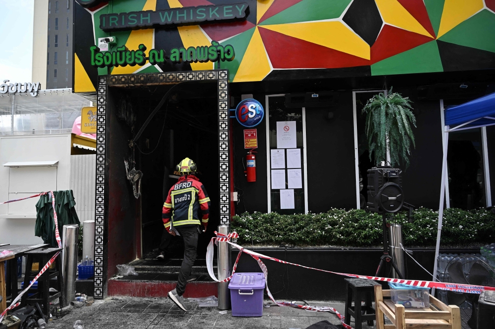  member of the Bangkok Fire and Rescue Department inspects the aftermath of a blaze inside the Rong Beer Na Lat Phrao bar in Bangkok