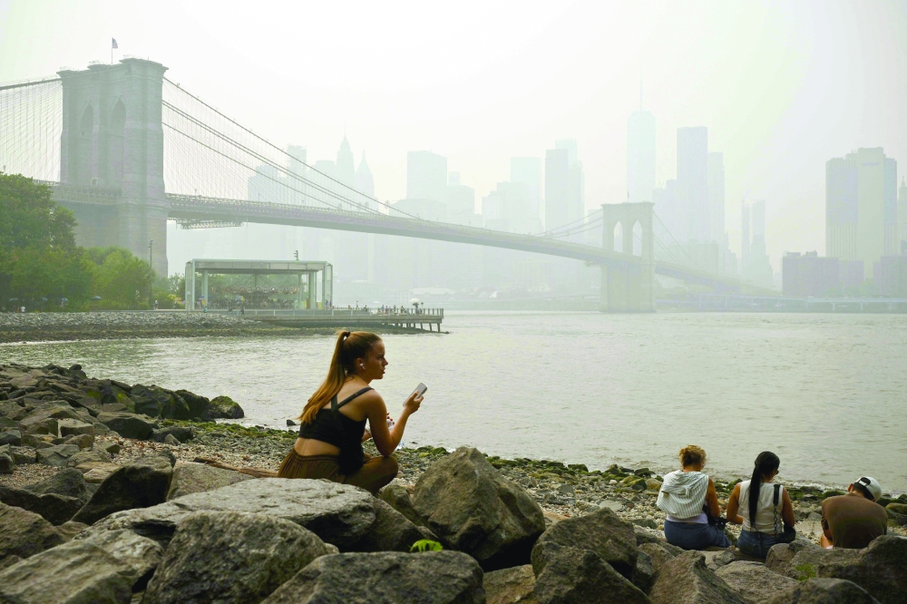 People sit near the Brooklyn Bridge as wildfire smoke from Canada causes hazy conditions in New York