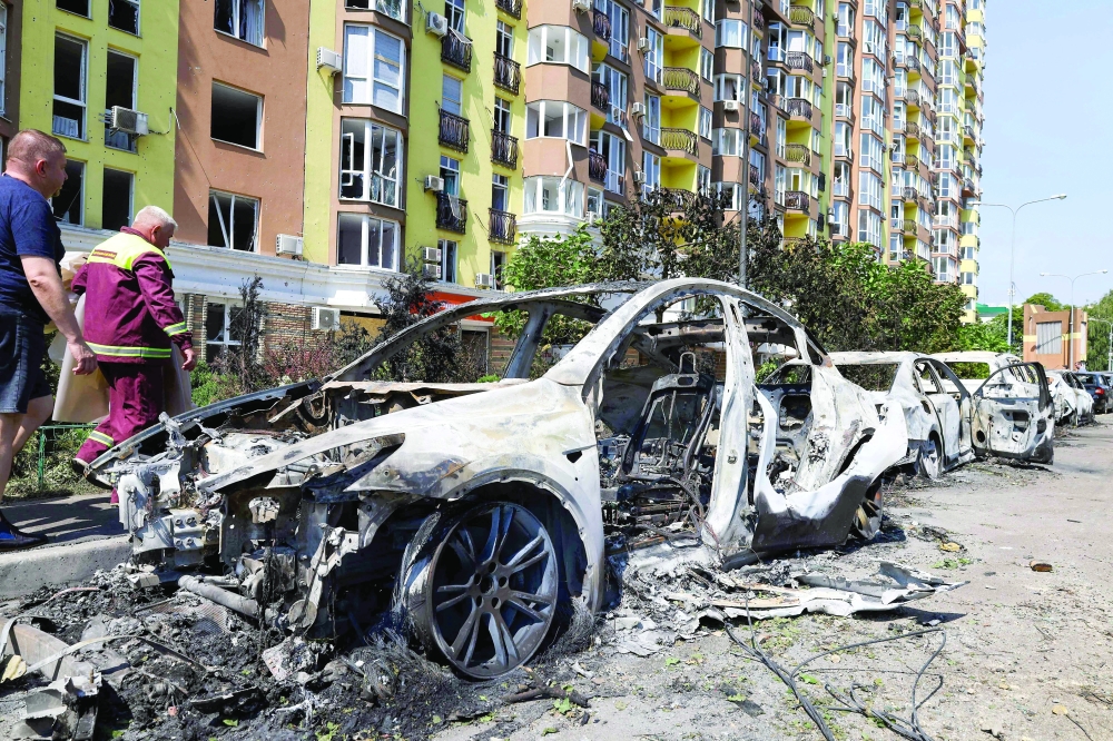 People walk past damaged cars parked in a street following missile strikes in Kyiv. — AFP