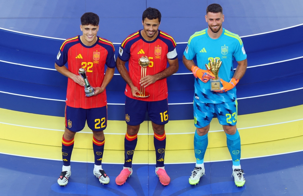  
Spain's Rodri celebrates on the podium after winning the Golden Ball with Golden Glove winner Unai Simon and FIFA Young Player winner Pau Cubarsi following winning the World Cup  