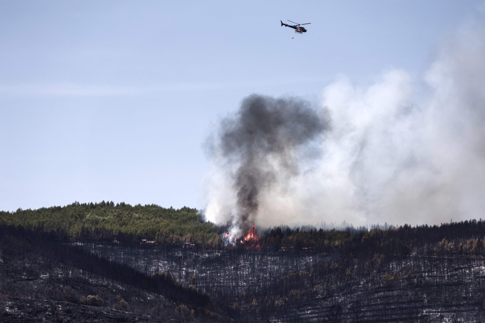 A helicopter flies after dropping water on a burning forest during a wildfire in Taradeau, southeastern France. — AFP