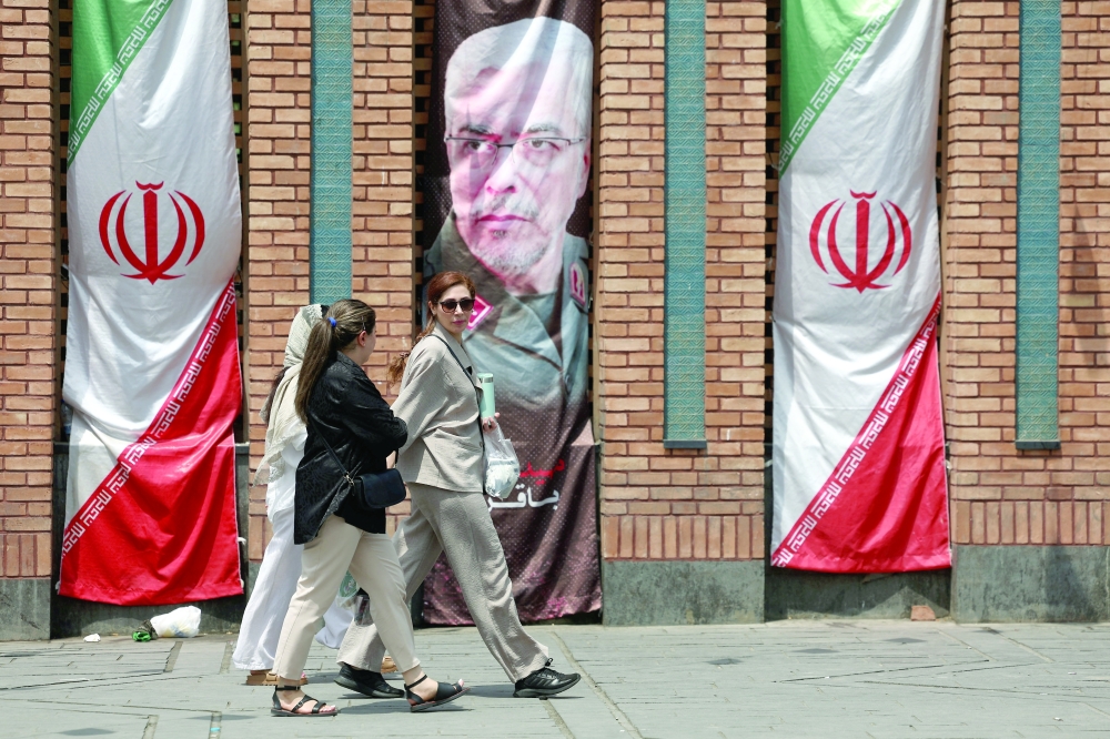 Iranian women walk past a banner with a picture of the former Chief of Staff of the Iranian Armed Forces, Mohammad Bagheri, in Tehran, Iran, on Monday. — Reuters