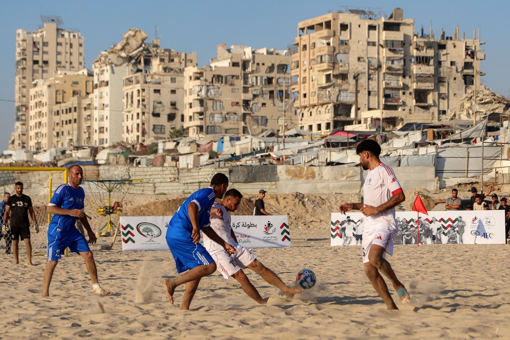 Palestinians from the Shati Team (blue) and the Gaza Sports Club (White) play in a beach football tournament along the beach in Gaza City