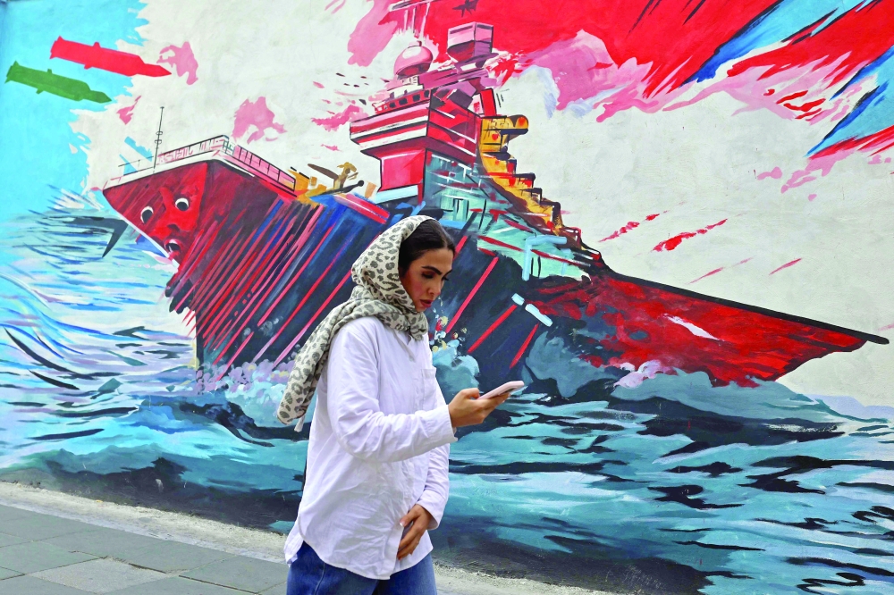 A commuter walks past a wall mural along the street in Tehran on Tuesday. — AFP