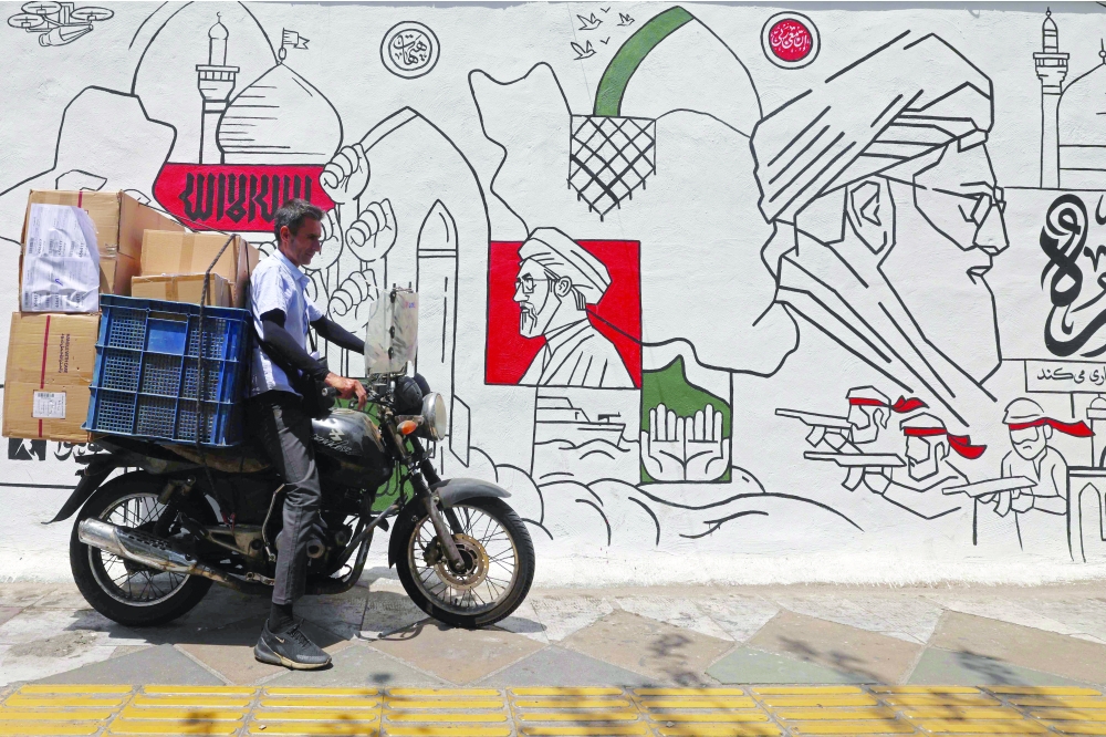 
A motorist parks his bike in front of a wall mural along the street in Tehran. — AFP 