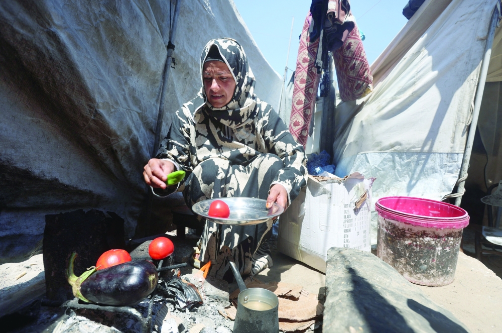 A displaced Palestinian woman cooks vegetables over a wood fire outside her tent, amid shortages of lighters and cooking gas, in Khan Yunis, in the southern Gaza Strip. —Reuters
