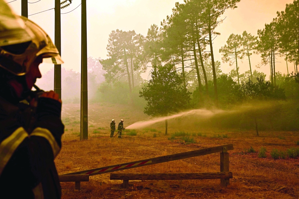 Firefighters spray water along the edge of a forest during a wildfire near the town of Lege-Cap-Ferret, in southwestern France. - AFP
