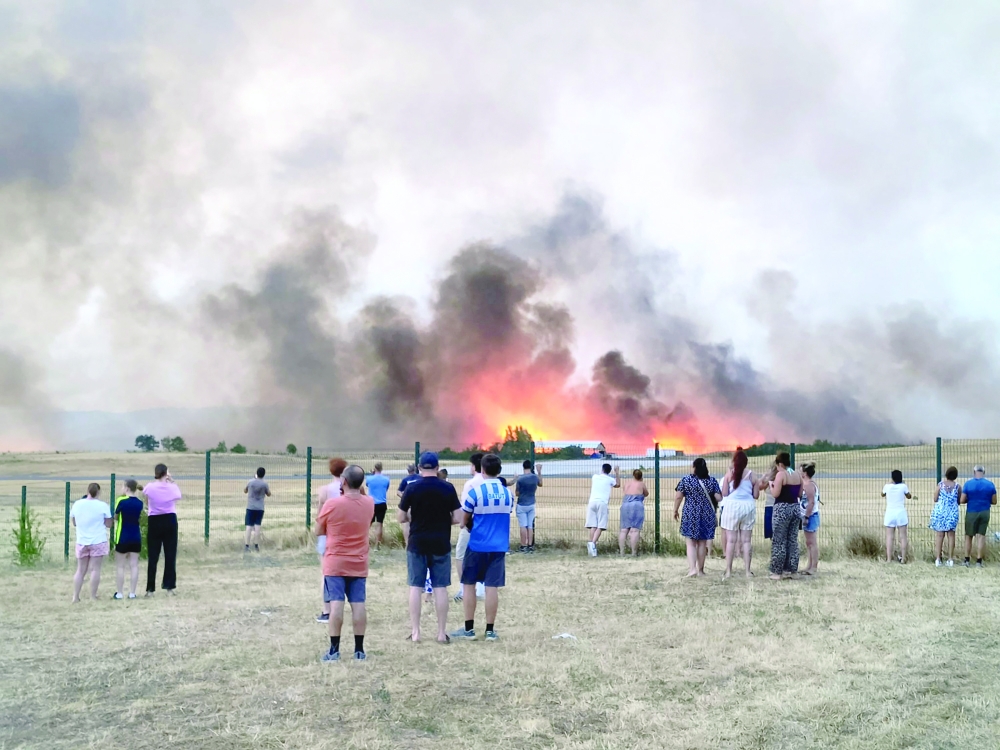 Bystanders look on as fire and smoke billow across Castres-Mazamet aerodrome, near Labruguiere in south-western France on July 24, 2026.  France and Spain evacuated more than 160,000 people as unprecedented forest fires ravaged areas on July 25, 2026, near Madrid and Bordeaux, a French city flanked by tourist havens and world-renowned vineyards. French President Emmanuel Macron asked the army to mobilise to help contain the worst wildfire the country has ever seen after seeking European Union help, as a local official warned the blaze was heading towards Bordeaux. (Photo by Daniel ABELOUS / AFP)
