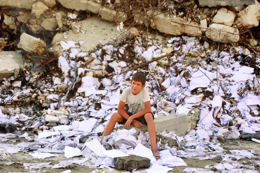 A Palestinian boy sits amid the debris of destroyed buildings following an Israeli strike at the Al-Jalaa street in Gaza City. — AFP