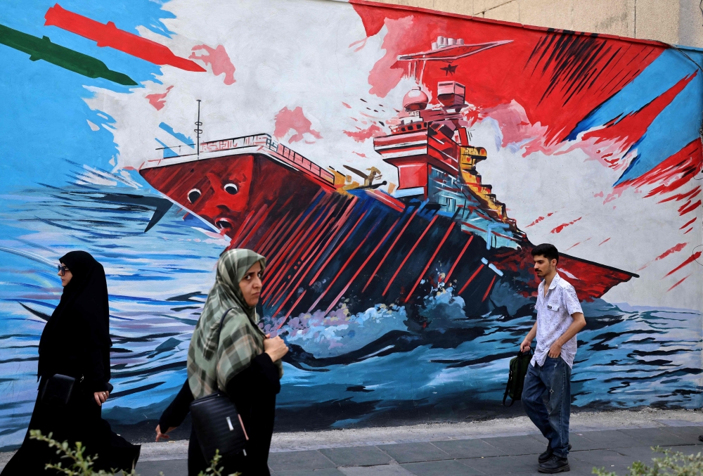 Commuters walk past a wall mural along the street in Tehran on July 21, 2026.