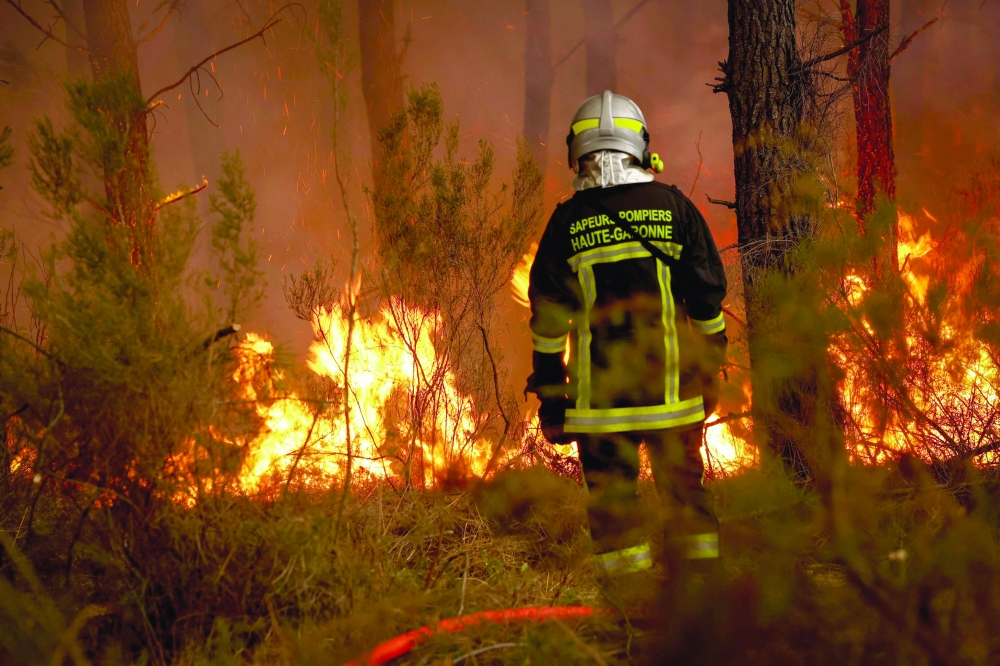 A firefighter stands before flames as a forest fire rages, some 30km from Bordeaux, France. — AFP
