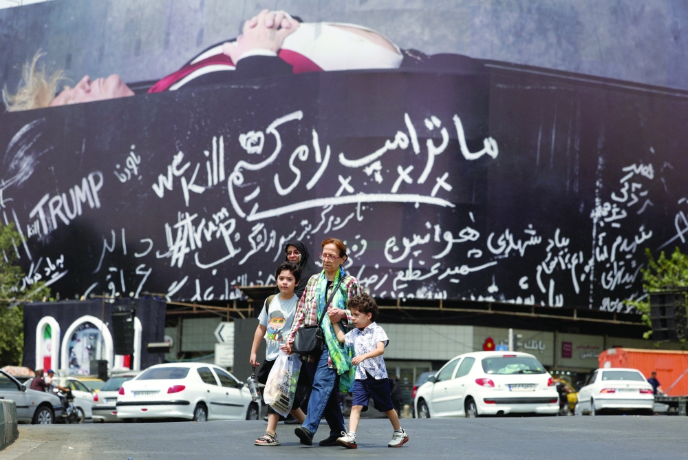 People cross the road past a huge war billboard, in Tehran