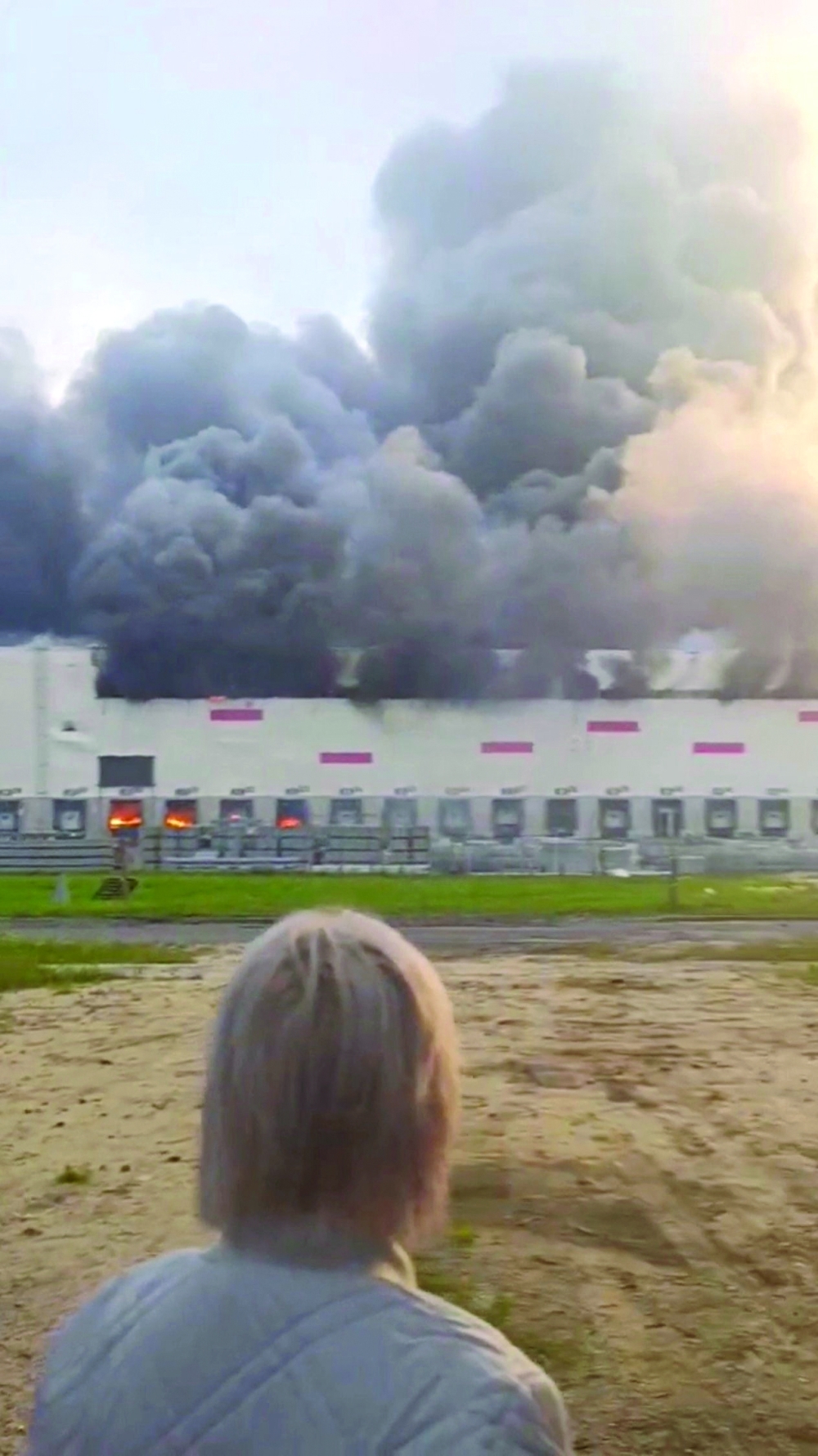 A woman looks on as smoke billows from a Wildberries warehouse after a fire broke out at the facility, in Ryazan region, Russia