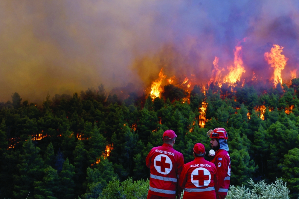 Members of the Hellenic Red Cross speak with each other, as smoke rises from a wildfire, in Krio Pigadi, Greece, August 1, 2026. REUTERS/Louisa Gouliamaki