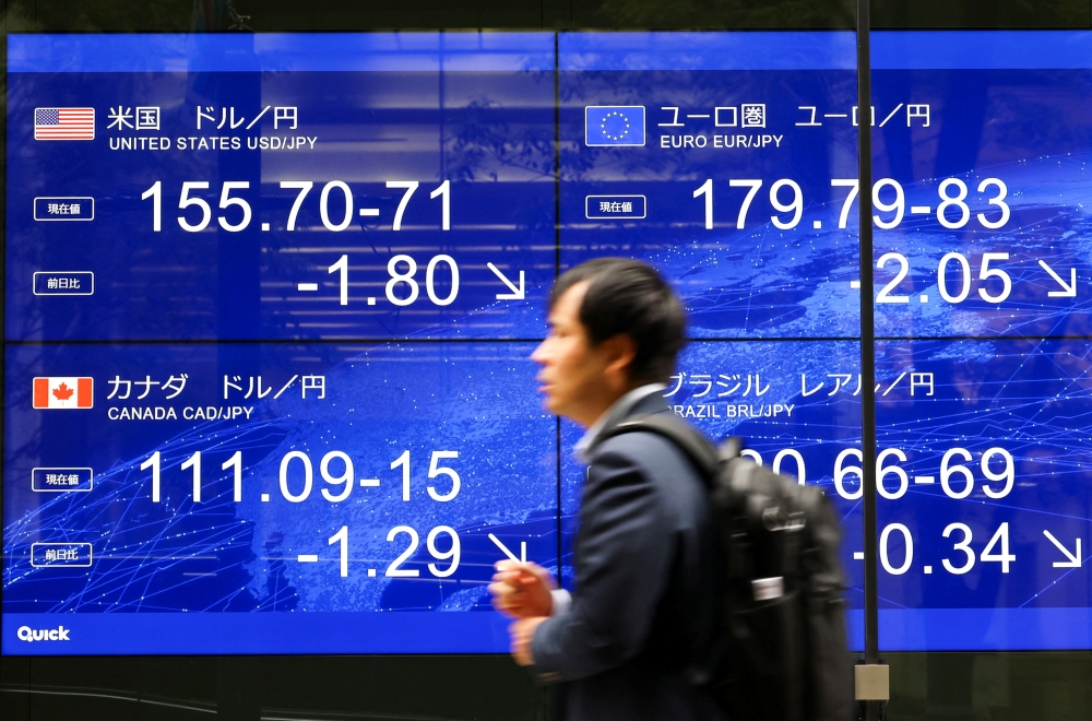 A man walks past an electronic screen displaying the current Japanese Yen exchange rate against the U.S. dollar 