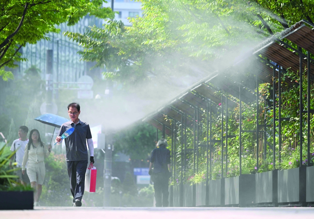 Pedestrians walk along a mist-spraying zone to cool off on a street in Seoul. — AFP