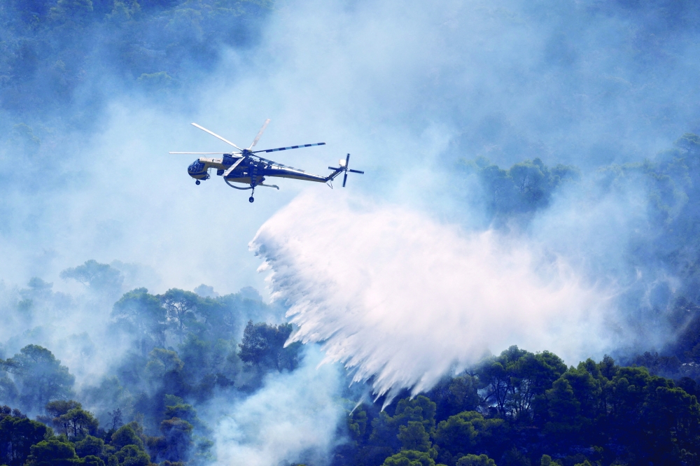 An Erickson firefighting helicopter makes strategic water drops as a wildfire burns in Mount Kitheronas, west of Athens. — Reuters 