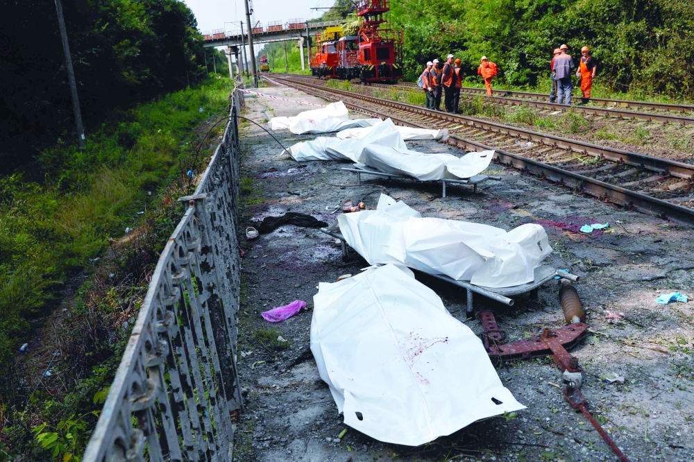 Railway workers gather on railway tracks next to bodies in plastic bags of people killed during Russian ballistic missile and drone strikes at a railway station in the Kyiv region on Wednesday. — AFP 