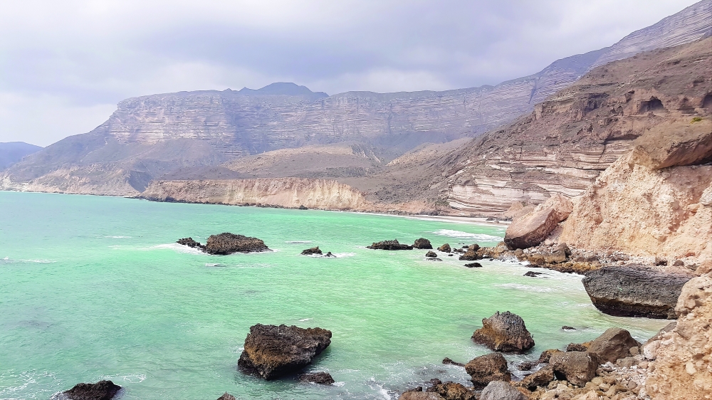 Dramatic layered cliffs above turquoise waters along the western coast near Al Fizayah
