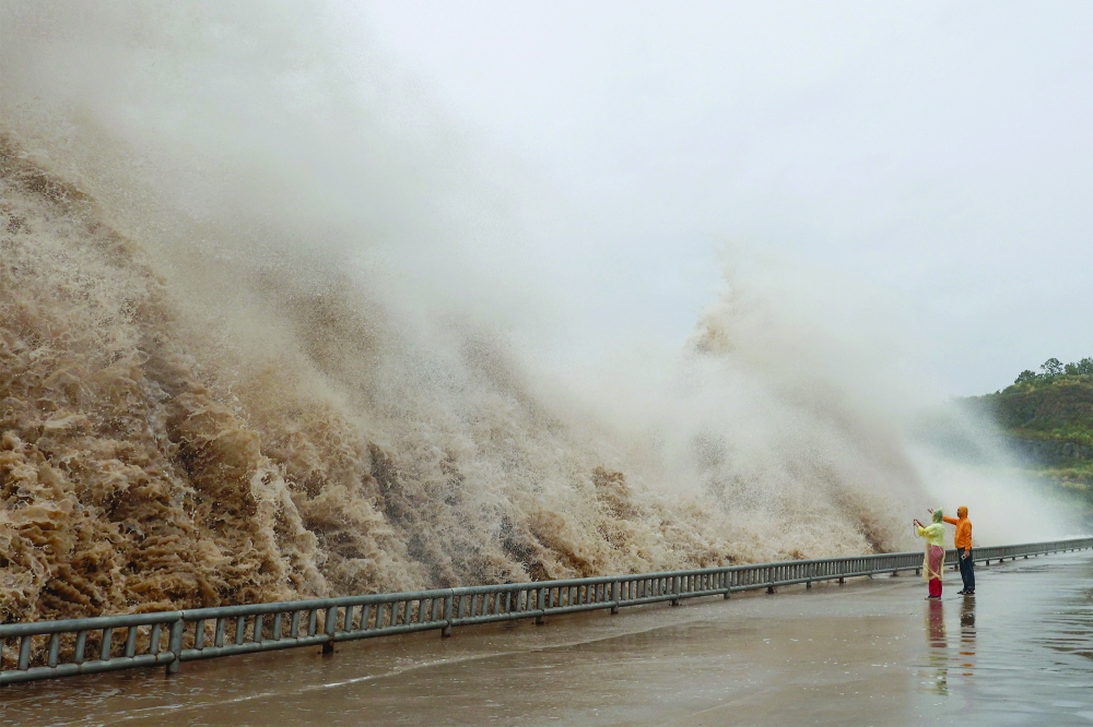 People stand next to huge waves crashing on a waterfront, in Sanmen County, China. — Reuters