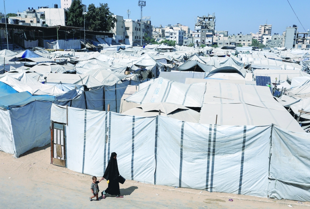 A Palestinian woman and a child walk next to a tent camp sheltering displaced Palestinians in Gaza City, August 9, 2026. REUTERS/Dawoud Abu Alkas