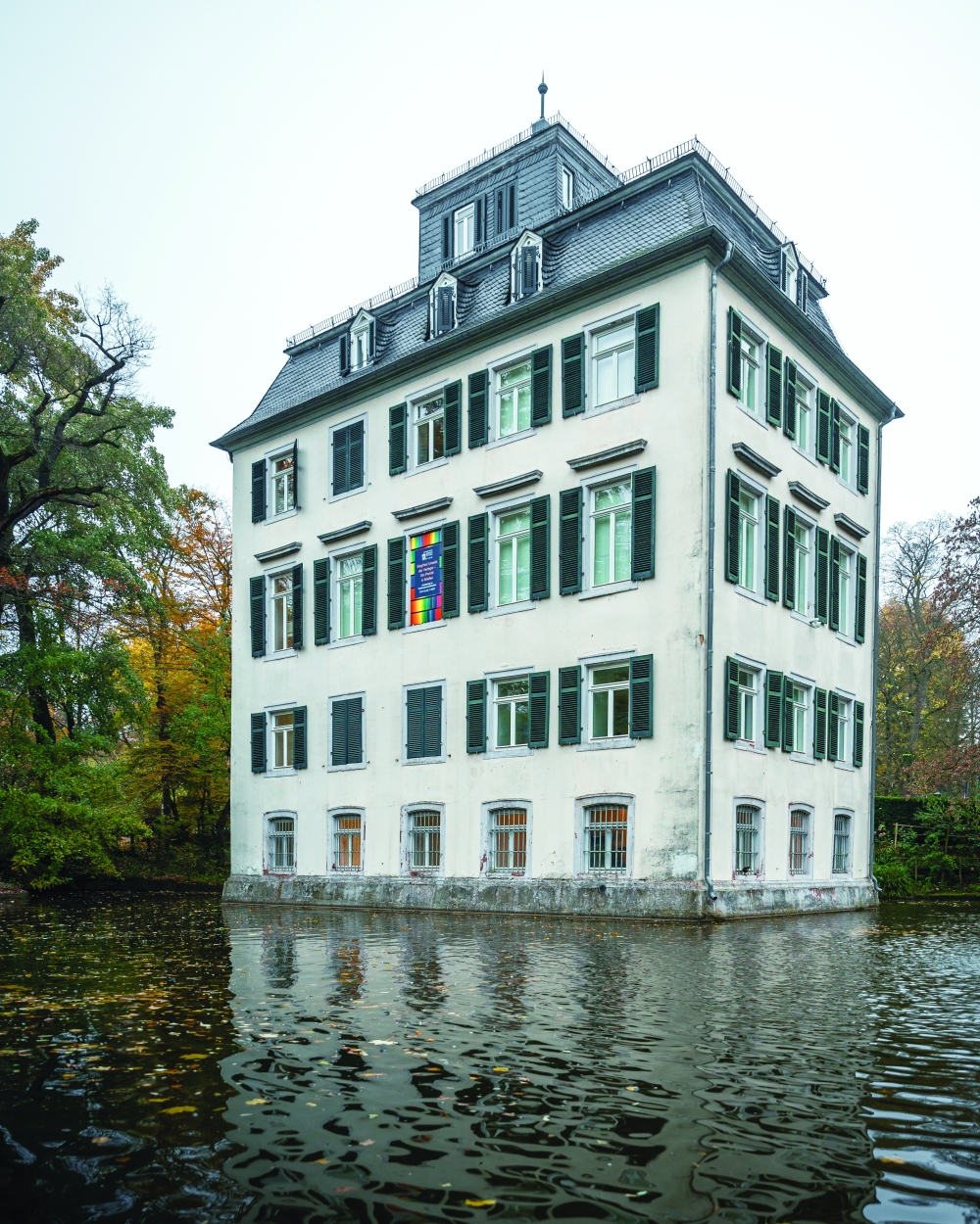 The historic Holzhausenschlösschen rising from its moat in Frankfurt’s Nordend, framed by autumn foliage under a soft grey sky.