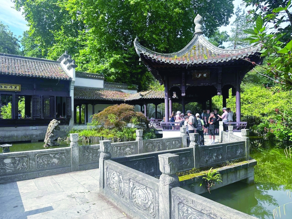 Visitors exploring the serene Chinese Garden in Bethmannpark, gathered by the Mirror Pavilion overlooking the peaceful pond