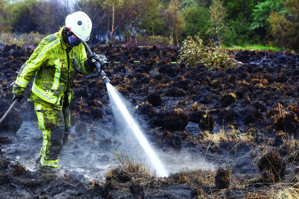 A Belgian firefighter sprays water in a field affected by a wildfire in Waimes, in the High Fens. — Reuters 