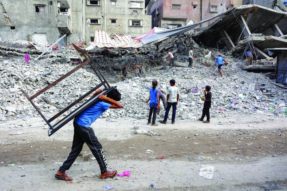 A boy walks carrying a table on his back past salvage workers scrapping the rubble of a building in Gaza. — AFP