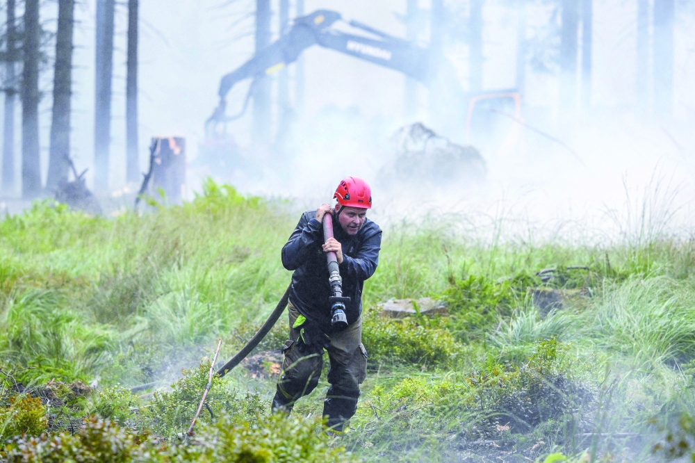 A firefighter carries a water hose as smoke emanates from burnt vegetation during operations against a wildfire at the Hautes Fagnes (High Fens). — AFP
