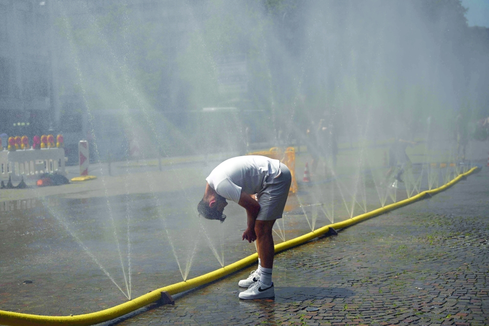 A man cools his head at water hoses spilling water to provide relief from the summer heat in Cologne, western Germany. — AFP