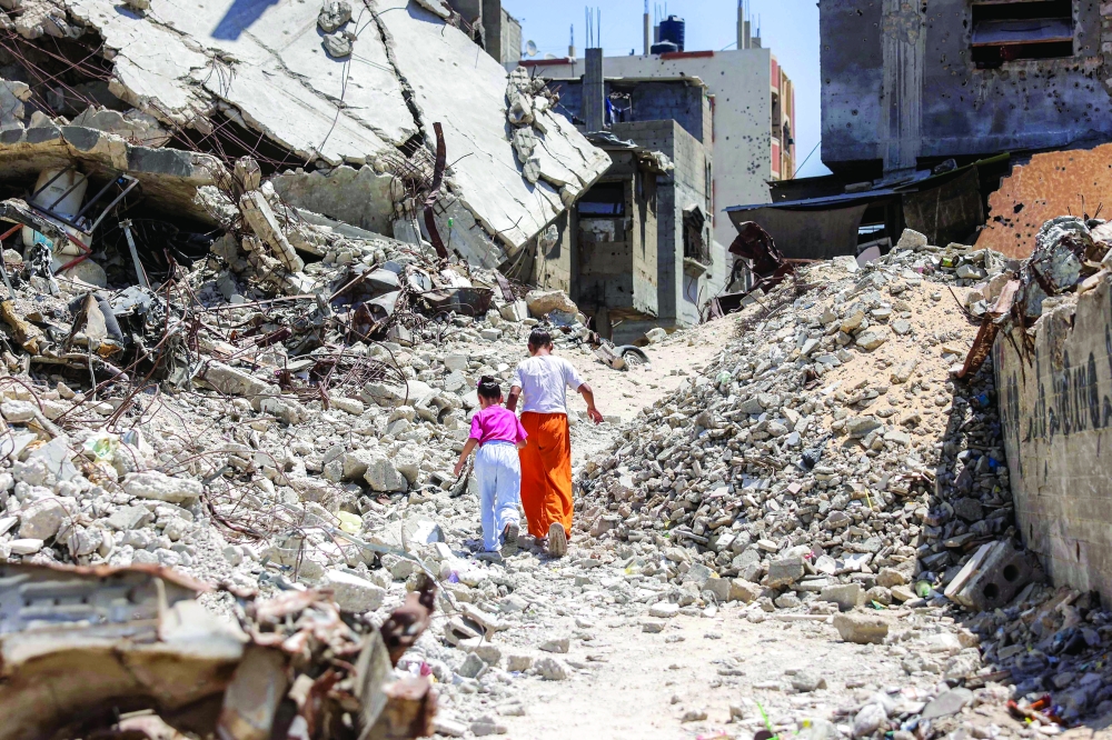 Two girls walk past the rubble of collapsed buildings in Khan Yunis in the southern Gaza Strip on August 25, 2026. A ceasefire in October 2025 has reduced but not halted the violence in Gaza. Israeli operations have killed 1,288 people since the ceasefire came into effect, according to Gaza's health ministry, which also operates under Hamas authority and whose figures are considered reliable by the United Nations. (Photo by Bashar Taleb / AFP)
