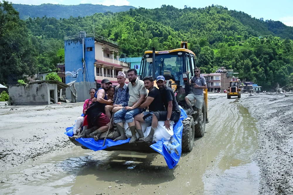 Rescue personnel transport stranded residents using a bulldozer after flash floods in the Devighat area in Nepal's Nuwakot district. - AFP
